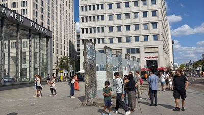 Tourists are shown at a square reading from the Berlin wall segments