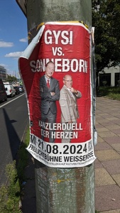 A red flyer is shown with two people in the center and the title “Gysi vs. Sonneborn”