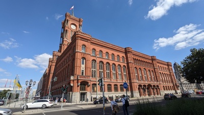 A red brick building is shown with a rigid square architecture and a flag on the top pole