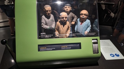 Four party leaders are shown as puppets in a box and a handle on the left can be triggered to make them raise their hands to show their support for a decision