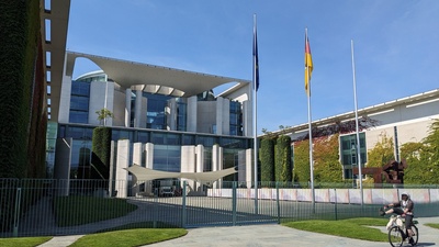 A modern government building with flags in front is shown