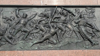 A metal illustration of soldiers storming from the left to the enemy on the righthand side