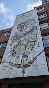 The side of a house depicts a graffiti with a man with a feather hat and holding a bow and arrow