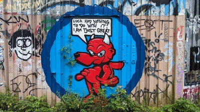 The side of a container with a grafitti is shown and the devil in the graffiti says “Luck had nothing to do with it! I am just great!”