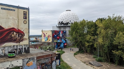 The foreground shows graffiti on buildings again but the back shows a building with a round white structure on top