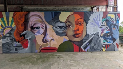 A colorful graffiti with two large visages are visible together with doves and a pen and a dog