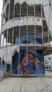 A tower with a ripped-apart outer fabric layer is shown and the ground floor shows a graffiti with a happy woman