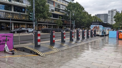 The entrance to the square is visible and in between walls some poles are placed in regular distance