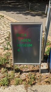 A post on the pavement with a black background and “Buchstabenmuseum” in green letters