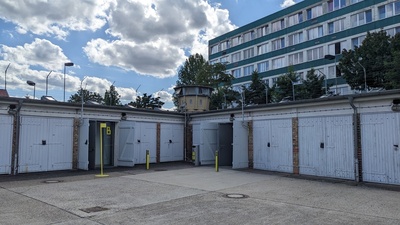 The photo shows the outermost layer of a prison with garage-like units with barbed fences on top