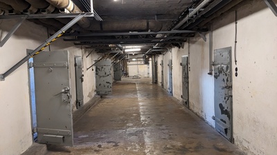 A lit hallway is shown and left and right are 5 metal prison cell doors each